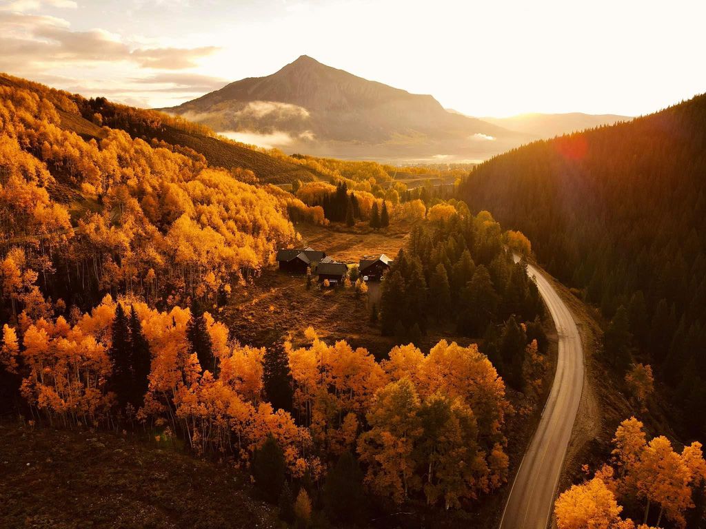 A road winding through golden fall aspens toward a mountain peak